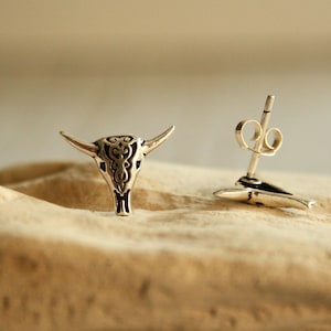 Può includere: Un paio di orecchini a bottone in argento con un design dettagliato di teschio di toro. Gli orecchini hanno una chiusura a perno e farfalla.