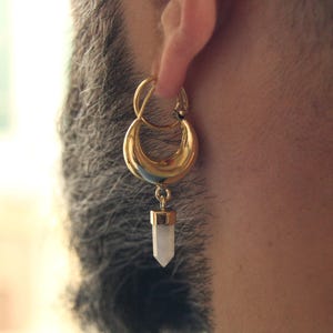 以下が含まれることがあります： ゴールドのフープイヤリングに、白いクリスタル製のペンダントがぶら下がっています。フープは二重リングのデザインです。