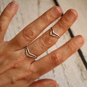 Könnte beinhalten: Zwei silberne Chevron-Ringe an der Hand einer Person. Die Ringe sind auf dem Mittelfinger übereinander gelegt.