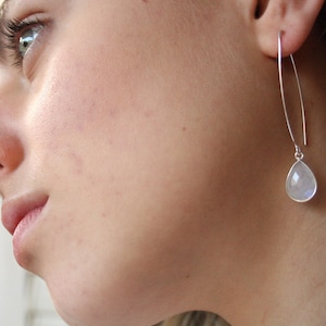 May include: A pair of silver dangle earrings with a teardrop-shaped moonstone pendant.