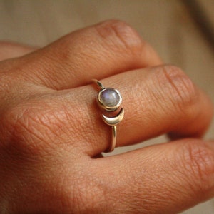 Könnte beinhalten: Ein silberner Ring mit einem Halbmond-Design und einem runden Mondstein.