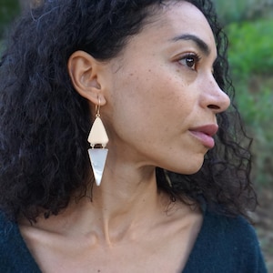 Puede incluir: Un par de pendientes geométricos de oro y plata con forma triangular. Los pendientes son colgantes y tienen un diseño en capas.