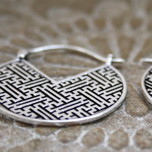 May include: A pair of silver hoop earrings with a geometric pattern. The earrings are made of metal and have a black and white design.