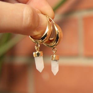 May include: Gold hoop earrings with a white crystal pendant hanging from each hoop.