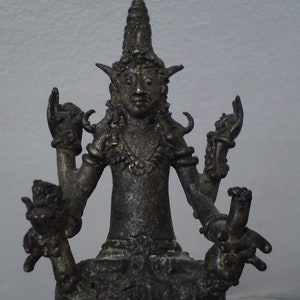 May include: A dark gray metal statue of a deity with four arms, wearing a crown and ornate jewelry. The statue is seated with its legs crossed and has a serene expression.