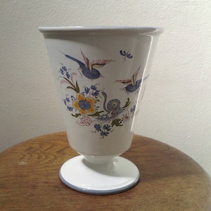 Könnte beinhalten: Eine weiße Keramikvase mit einem blauen und gelben Blumendesign und drei blauen Vögeln. Die Vase hat einen Sockel.