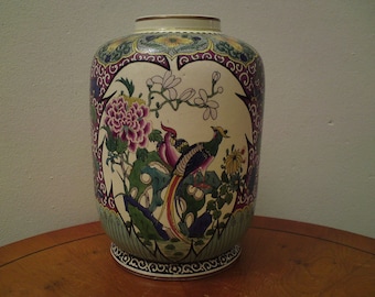 May include: A white ceramic vase with a floral and bird design. The vase has a round body and a narrow neck. The design features pink, purple, green, and yellow flowers, as well as two birds with blue, green, and yellow feathers.
