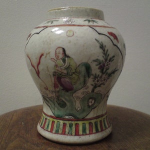 Könnte beinhalten: Eine weiße Porzellanvase mit einem bauchigen Körper und einem schmalen Hals. Die Vase ist mit handbemalten floralen und figürlichen Motiven in Rot-, Grün- und Blautönen verziert.