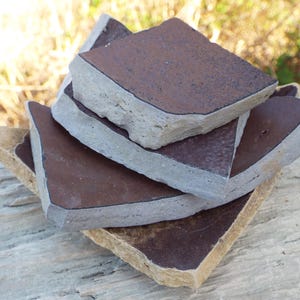 May include: A stack of four brown ceramic tiles with a light grey rim. The tiles are stacked on a wooden surface.