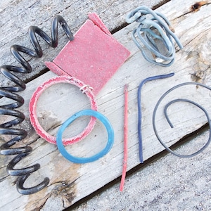 May include: A collection of assorted craft supplies including a red sanding block, a black spring, a blue and red ring, a blue ring, a red stick, a blue wire, and a black wire.