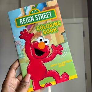 May include: A colourful colouring book titled "Reign Street Coloring Book" featuring a cartoon character. The cover has a green and yellow border with the text "Happy 2nd Birthday Reign!"