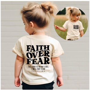 Puede incluir: Una camiseta beige claro para ni&ntilde;os peque&ntilde;os con texto negro que dice "FAITH OVER FEAR" y "THE LORD IS ON MY SIDE; I WILL NOT FEAR PSALMS 118:6".