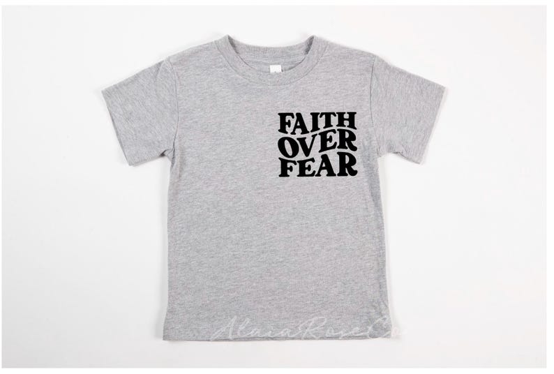 Puede incluir: Una camiseta gris de manga corta con el texto "FAITH OVER FEAR" impreso en negro en la parte delantera.