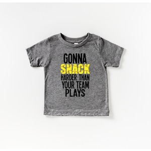 May include: Gray short-sleeved t-shirt with the text "Gonna Snack Harder Than Your Team Plays" in black with a yellow softball graphic.