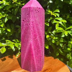 May include: A large, pink, crystal-shaped candle with a textured surface. The candle is sitting on a wooden surface.