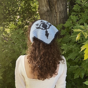 Puede incluir: Una persona lleva una bandana azul claro con un diseño en blanco y negro. La bandana está atada alrededor de la cabeza y cubre el cabello. La persona lleva un top blanco corto y pantalones vaqueros azules.