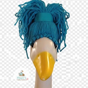 May include: A white goose statue head wearing a bright teal yarn wig styled into a messy bun. The text MESSY BUN appears above the head, and PORCH GOOSE CLUB appears below. A small logo for Maw's Crafty Creations is visible on the lower left side.