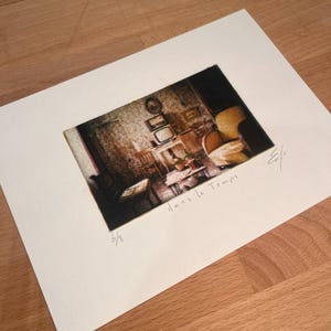 May include: A framed print of an interior scene, featuring a vintage aesthetic. The artwork depicts a room with furniture, a television, and the text "Dans le Temps". The print is numbered 6/8.