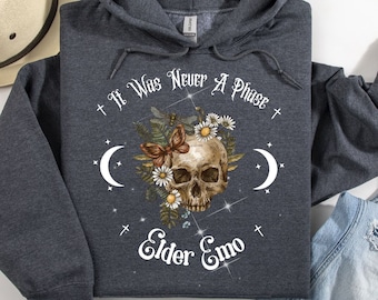 May include: A dark gray hooded sweatshirt with the text "It Was Never A Phase + Elder Emo +" printed on the front. The text is surrounded by a skull with flowers, butterflies, and moons.