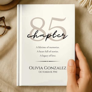 May include: A white hardcover book with the large grey number 85 and the word chapter in black script. The text reads: A lifetime of memories. A heart full of stories. A legacy of love. OLIVIA GONZALEZ OCTOBER 8, 1941 is printed at the bottom.