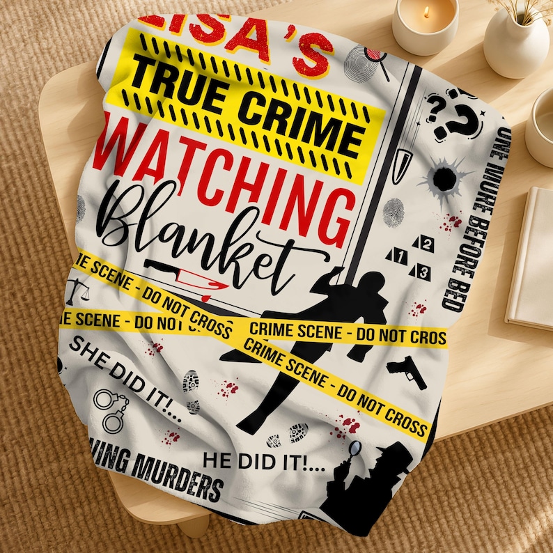 May include: A cream-coloured blanket with a crime scene theme. The blanket features the text "LISA'S TRUE CRIME WATCHING Blanket" in red and black, along with crime scene tape, silhouettes, and other crime-related graphics.