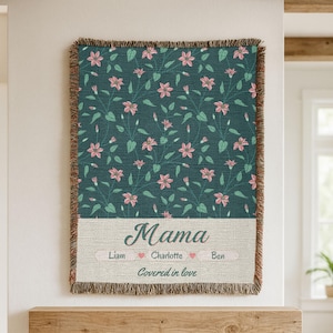 Pu&ograve; includere: Una coperta tessuta con un motivo floreale verde acqua e bordi sfrangiati. La coperta presenta la parola "Mama" in corsivo, con nomi e la frase "Covered in love" sotto.