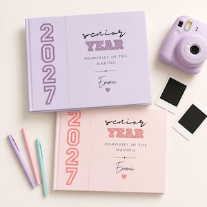 May include: Two rectangular photo albums in light purple and light pink, featuring the text 2027, senior YEAR, MEMORIES IN THE MAKING, and the name Emma with a heart. Includes a light purple instant camera, two blank photo frames, and three pens.