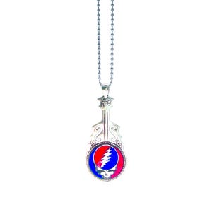 May include: A silver-colored pendant necklace featuring a stylized violin shape. The pendant has a circular emblem with a red, blue, and pink design of a skull and lightning bolt. The necklace has a ball chain.