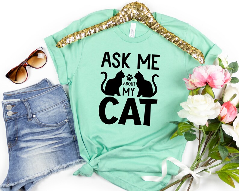 Może przedstawiać: Mint zielony t-shirt z czarnym tekstem, kt&oacute;ry brzmi "Ask me about my cat" i dwie czarne sylwetki kot&oacute;w.