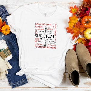 May include: White t-shirt with a red and black word cloud design that says "Surgical Tech". The design includes words like "commitment", "loyalty", "trust", "know-how", "dedicated", and "compassionate".