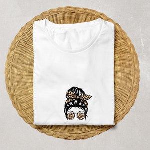 Op de afbeelding: Wit T-shirt met een afbeelding van een vrouw met een rommelige knot, zonnebril en een haarband met luipaardprint.