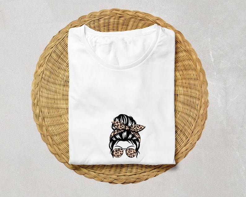 Op de afbeelding: Wit T-shirt met een afbeelding van een vrouw met een rommelige knot, zonnebril en een haarband met luipaardprint.