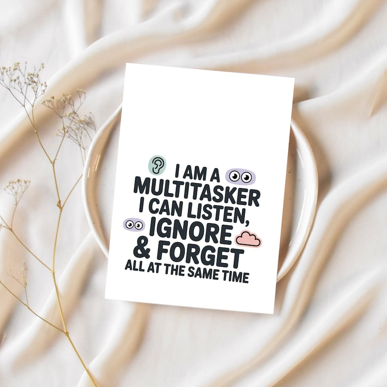 K&ouml;nnte beinhalten: Eine wei&szlig;e Karte mit dem Text "I AM A MULTITASKER I CAN LISTEN, IGNORE & FORGET ALL AT THE SAME TIME" in Schwarz, T&uuml;rkis und Lila. Die Karte liegt auf einem wei&szlig;en Teller und einem beigen Stoff.