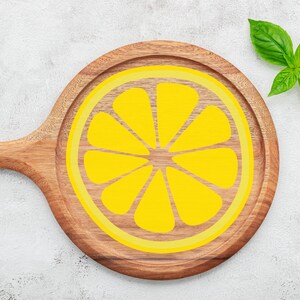 Puede incluir: Una tabla de cortar de madera con un dise&ntilde;o de lim&oacute;n amarillo. La tabla tiene un mango y es redonda.