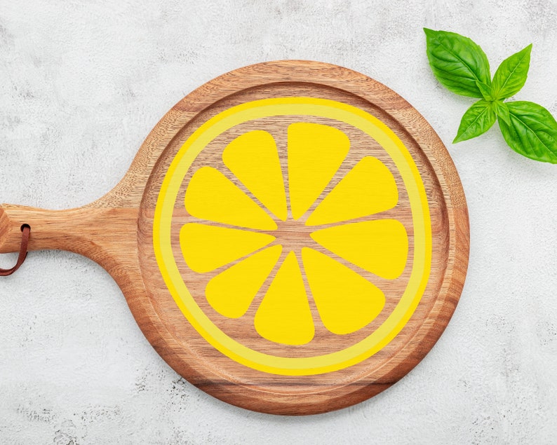 Puede incluir: Una tabla de cortar de madera con un dise&ntilde;o de lim&oacute;n amarillo. La tabla tiene un mango y es redonda.