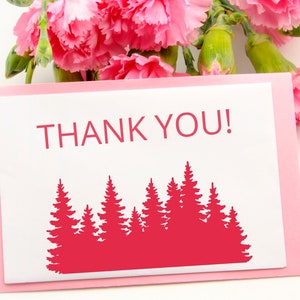 May include: A pink card with a white border and the text "THANK YOU!" in red. A red silhouette of a forest of pine trees is below the text.