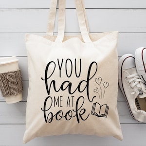 May include: A white canvas tote bag with black text that reads "You had me at book" with a small illustration of a book and three hearts.