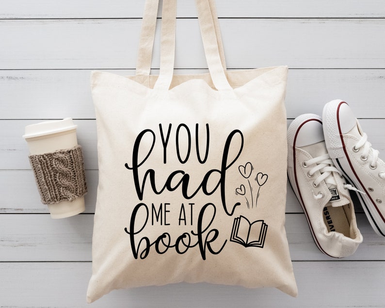 May include: A white canvas tote bag with black text that reads "You had me at book" with a small illustration of a book and three hearts.