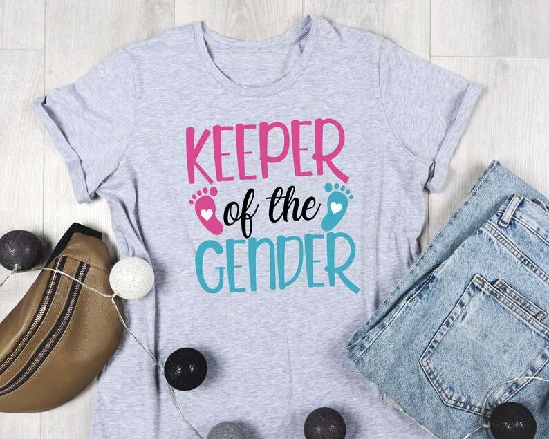 May include: Grey t-shirt with the text "KEEPER of the GENDER" in pink and blue lettering. The text is surrounded by two blue and pink footprints with white hearts.