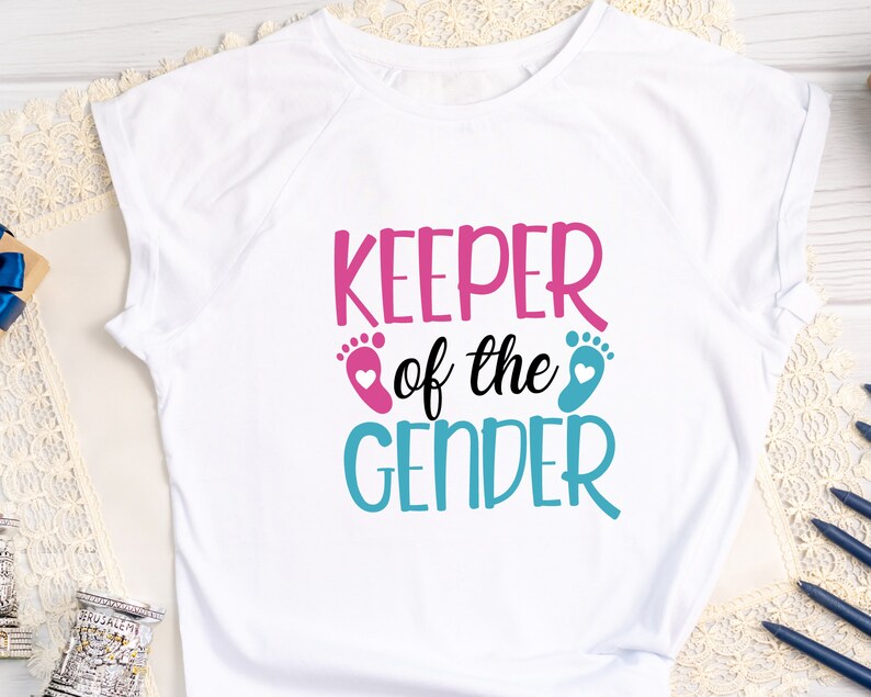 May include: White t-shirt with the text "Keeper of the Gender" in pink and blue with a pink and blue footprint on either side of the text.