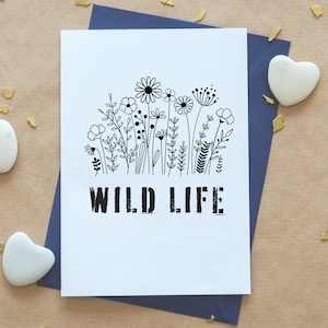 Puede incluir: Una tarjeta blanca con una ilustraci&oacute;n en blanco y negro de un campo de flores silvestres. El texto "WILD LIFE" est&aacute; impreso en negro debajo de la ilustraci&oacute;n.