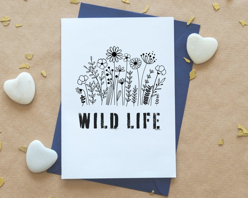 Puede incluir: Una tarjeta blanca con una ilustraci&oacute;n en blanco y negro de un campo de flores silvestres. El texto "WILD LIFE" est&aacute; impreso en negro debajo de la ilustraci&oacute;n.