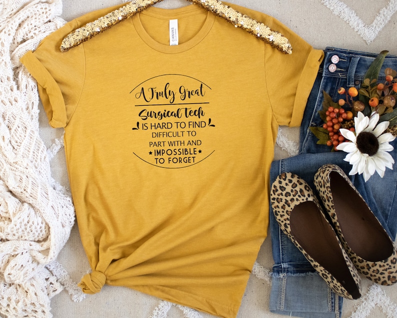 May include: A mustard yellow t-shirt with black text that reads "A Truly Great Surgical Tech is hard to find, difficult to part with and *impossible* to forget".