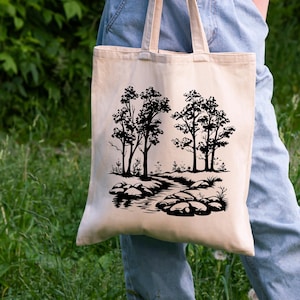 May include: A beige tote bag with black silhouette artwork of trees and a stream. The artwork features a winding stream with rocks and foliage.