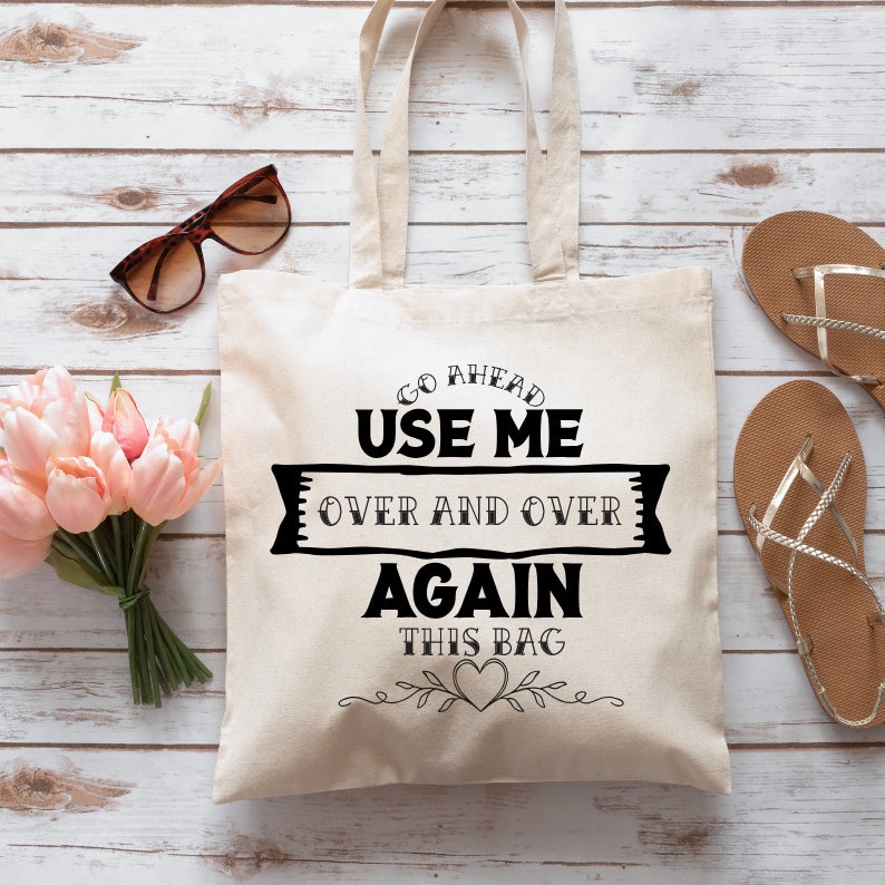 May include: A white canvas tote bag with black text that reads "Go Ahead Use Me Over and Over Again This Bag" with a heart and floral design.