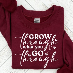 May include: Burgundy sweatshirt with white text that reads "GROW through what you GO through" with small hearts around the text.