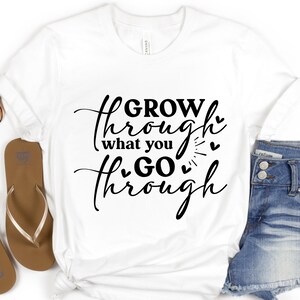 May include: White t-shirt with black text that reads "GROW through what you GO through" with small hearts around the text.