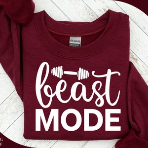 Op de afbeelding: Een maroon sweatshirt met de tekst "beast MODE" in witte letters. De tekst wordt vergezeld door een witte haltergrafiek.