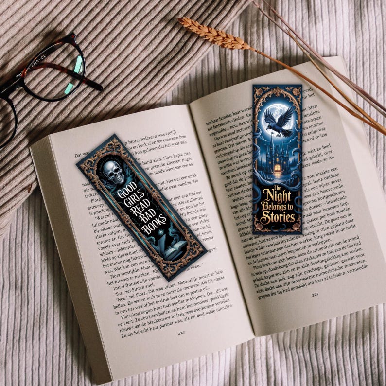 May include: Two decorative bookmarks with gothic designs rest on an open book. One bookmark features a skull and the text "GOOD GIRLS READ BAD BOOKS." The other shows a crow, a castle, and the text "The Night Belongs to Stories."