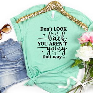 May include: Mint green t-shirt with black text that reads "Don't look back you aren't going that way..."